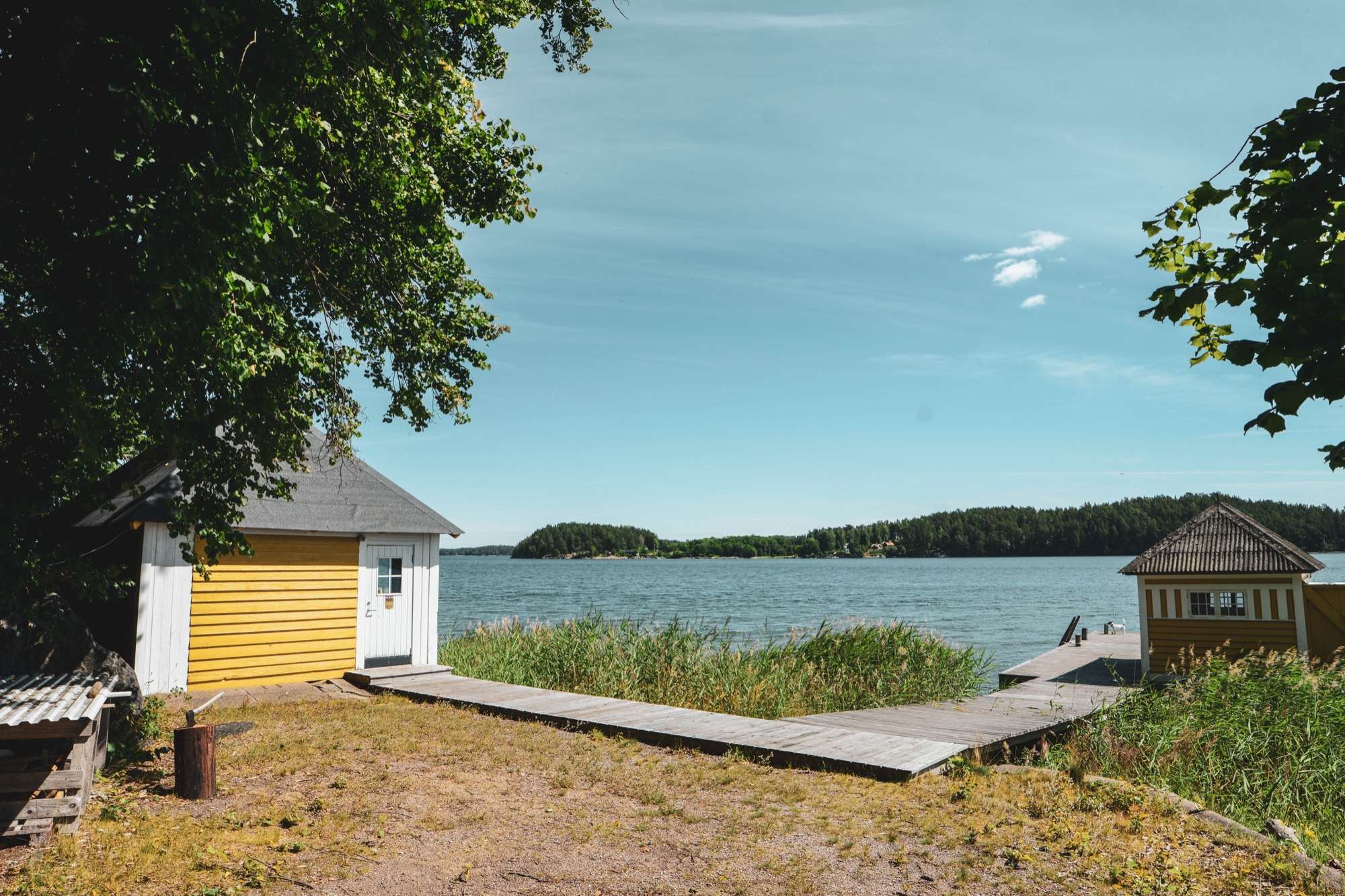 Gula byggnader vid stranden, en trätrall ut till bryggan och öppet vatten med skogsklädda öar bortom.